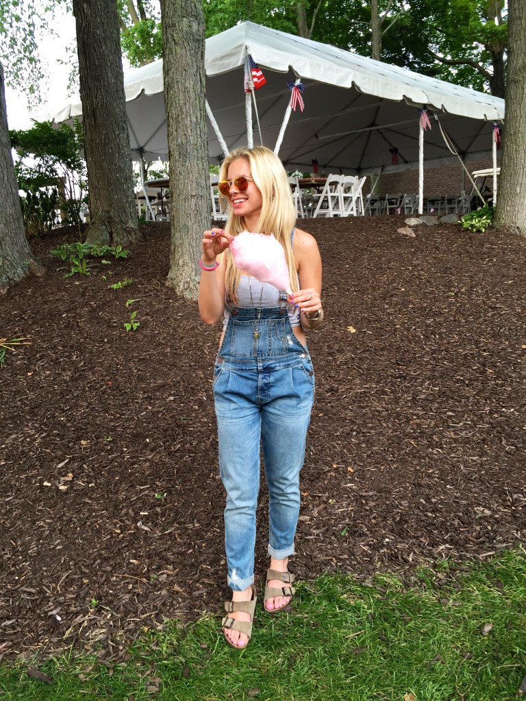 distressed overalls and tan birkenstock sandals, circle mirrored ray-ban sunglasses, girl eating cotton candy